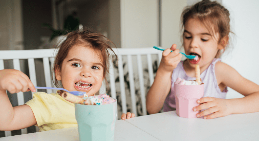 Two preschool girls sitting at table eating ice cream out of cups