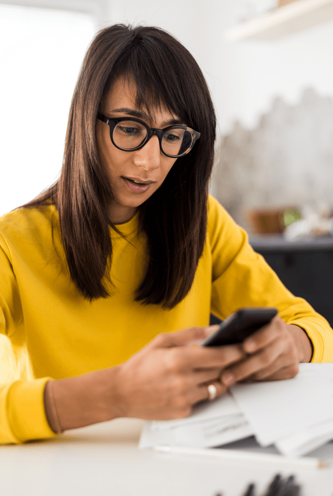 woman with brown hair and glasses looks at phone in her hand