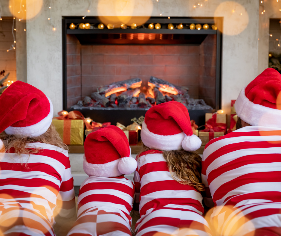 4 kids in striped pajamas and Santa hats lie on ground facing fire place