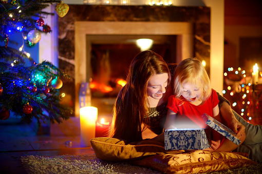 happy woman and daughter opening a gift beside Christmas tree 