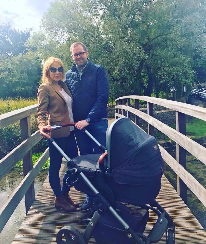 couple embracing the baby years with their stroller on a bridge