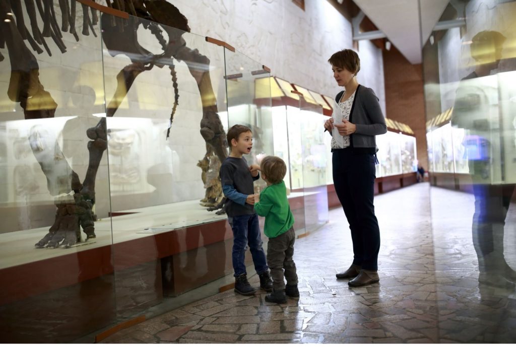 a woman and two boys in a museum standing next to dinosaur skeleton