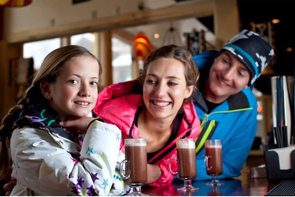 parents and daughter in winter gear enjoying hot chocolate