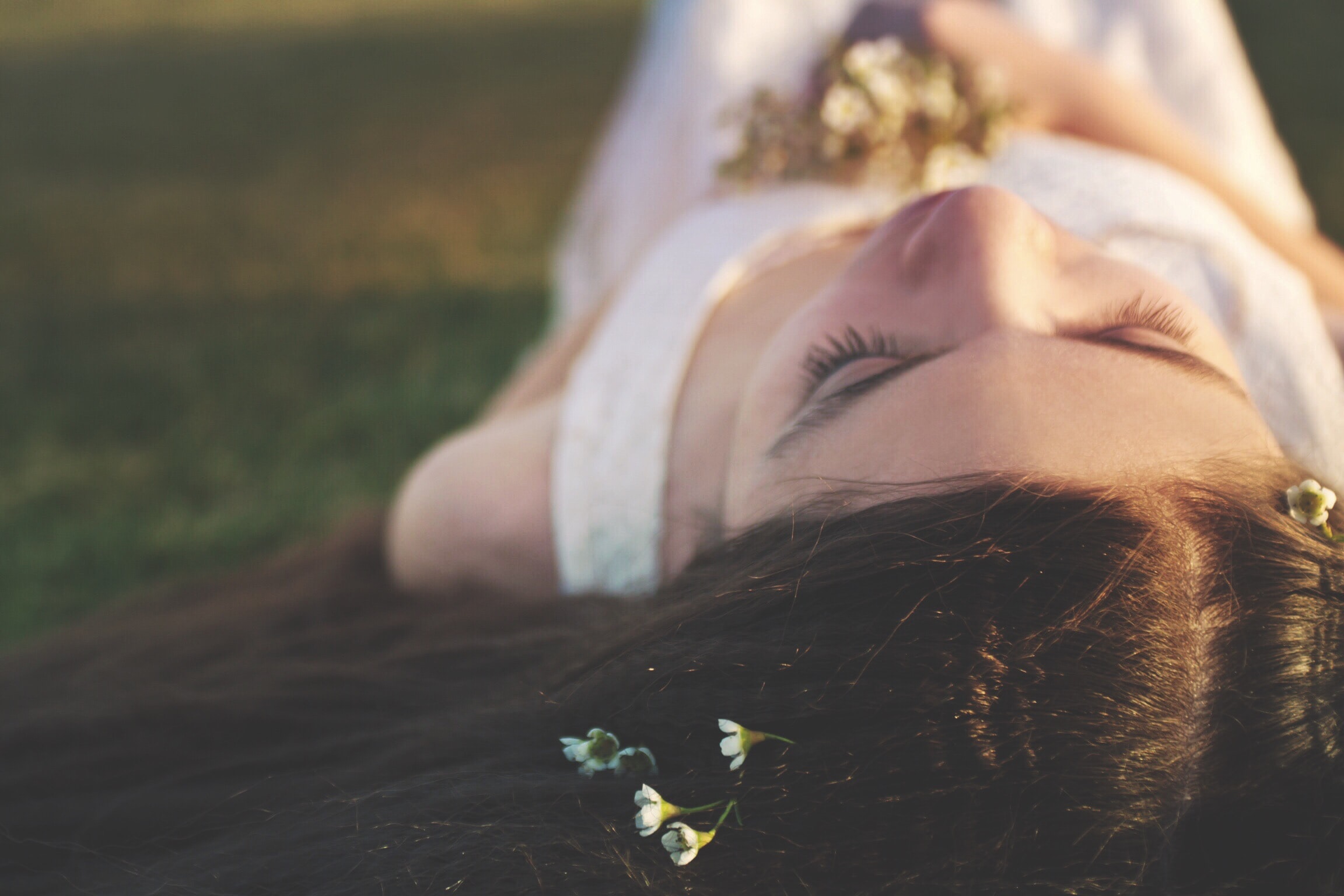 woman with flowers in hair lies on grass with eyes closed, manifesting her desires