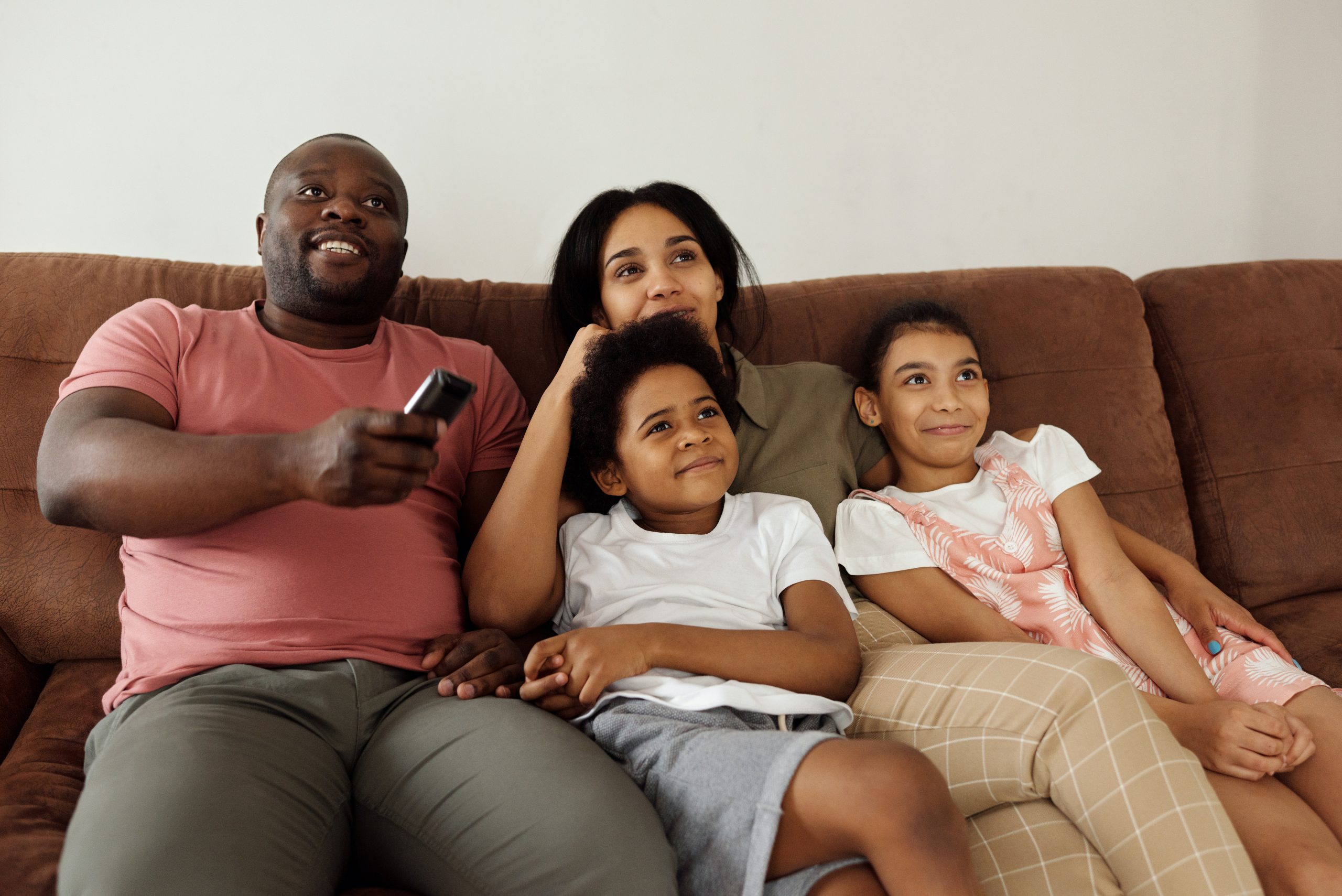 mom, dad and 2 kids lounge on couch watching tv