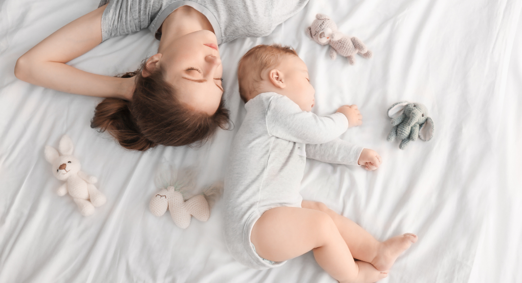woman and infant asleep on white sheet