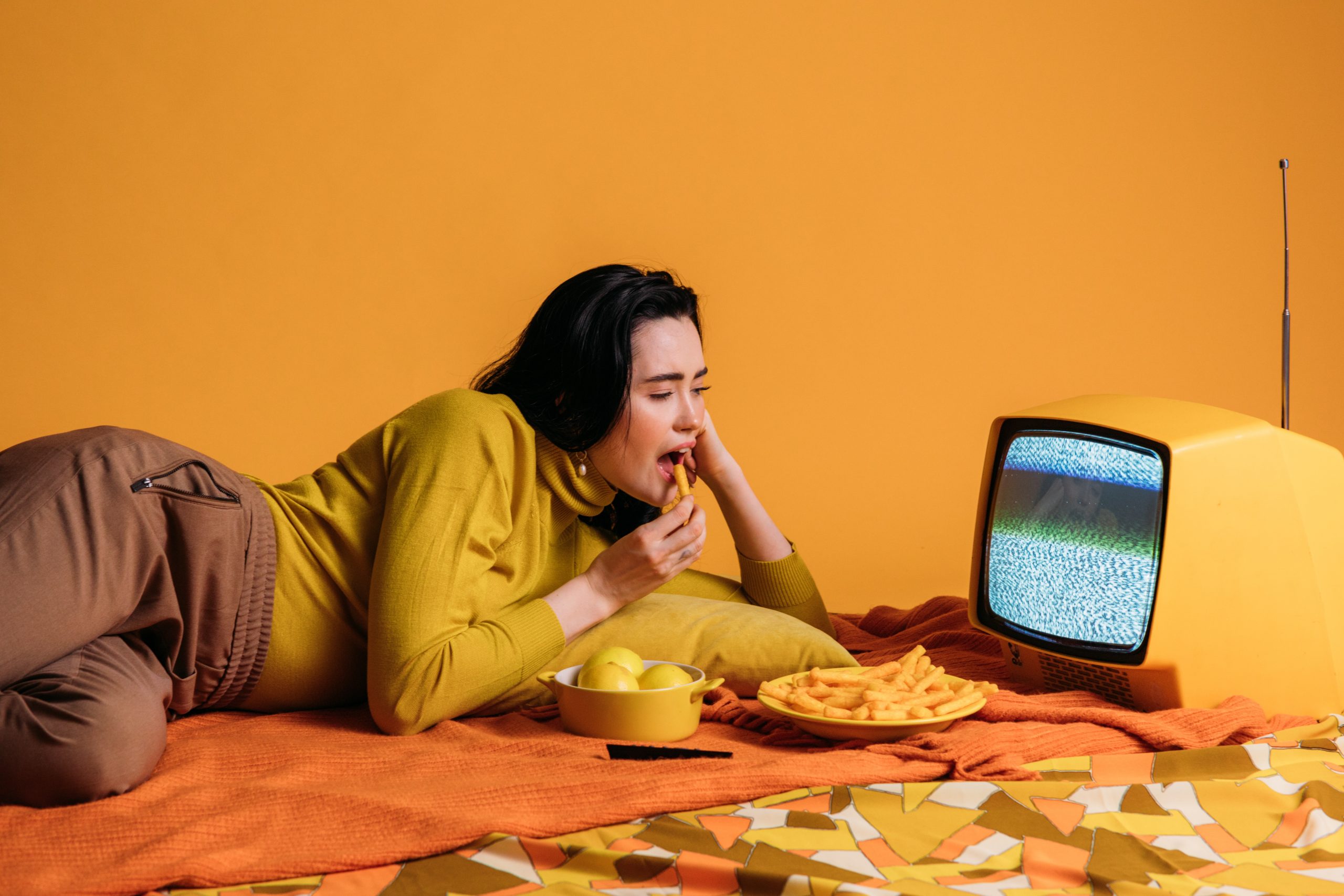 woman lies on bed with snacks watching tv