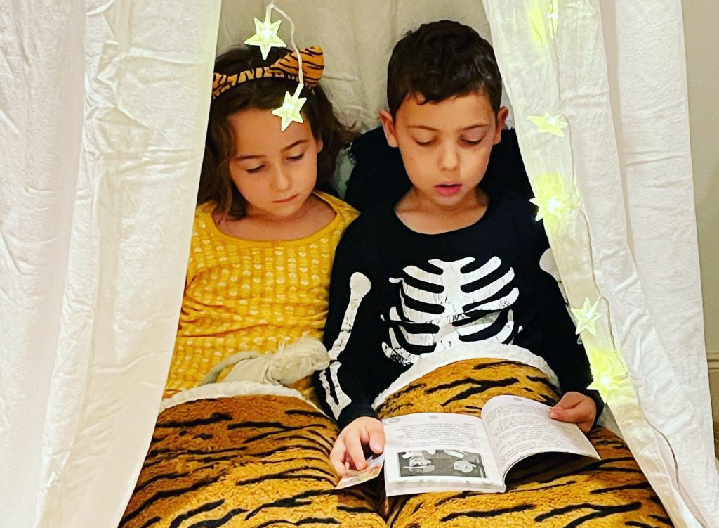 brother and sister reading a book together under a canopy
