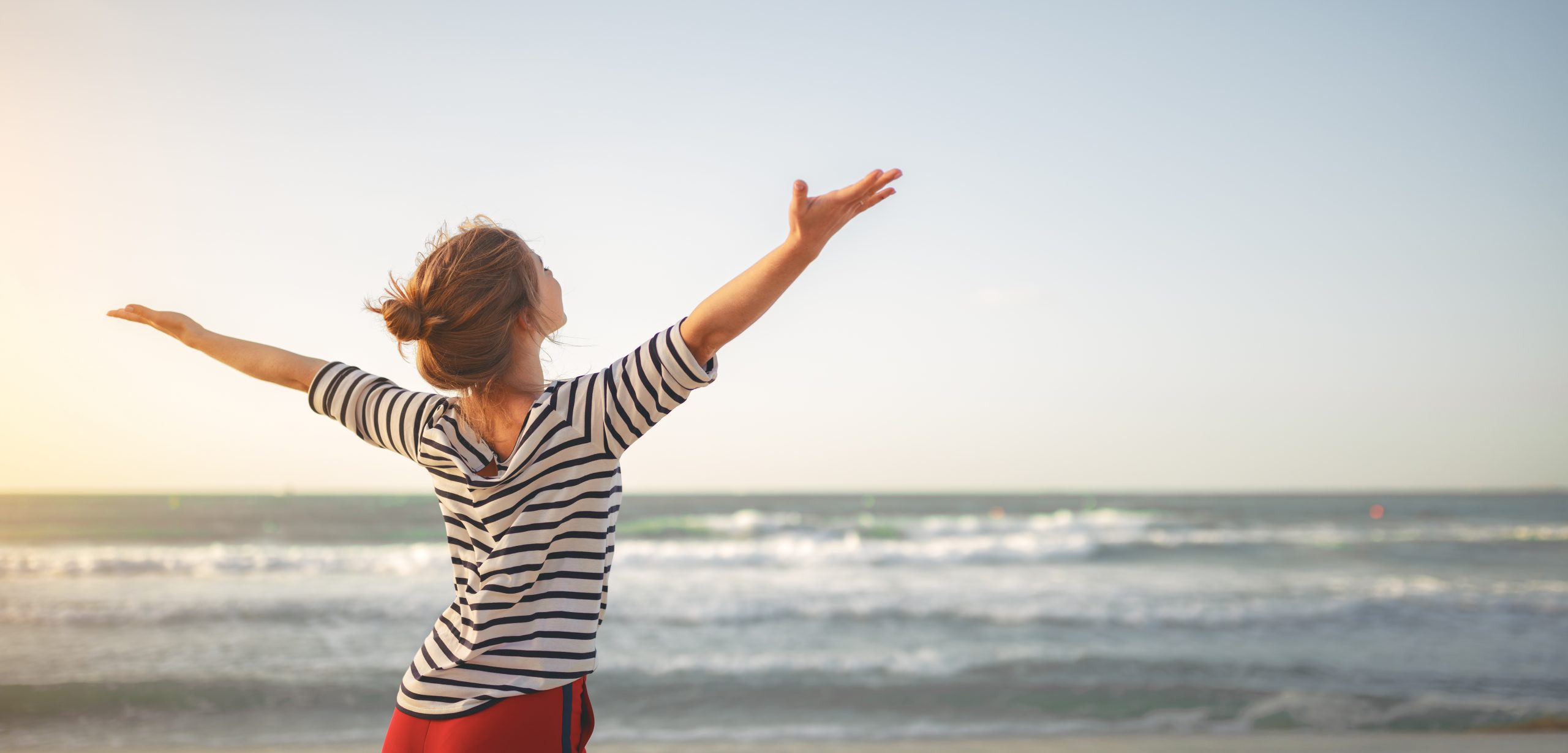 woman standing in front of the ocean with arms outstretched in victory stance