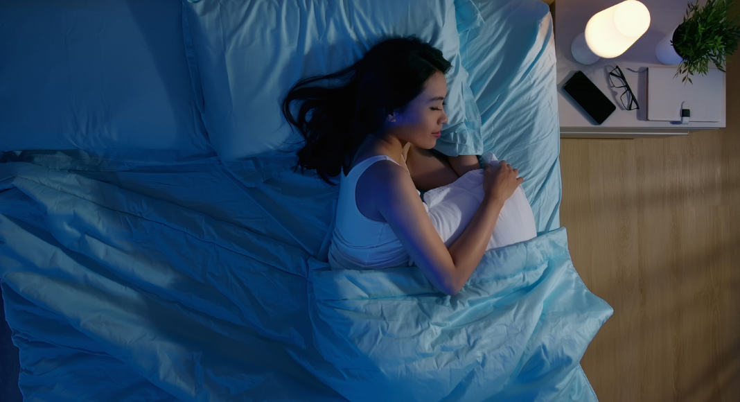 woman getting sleep on side of bed with nightlight on bedside table