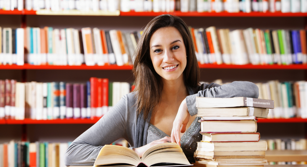 woman at library sits with stack of books 