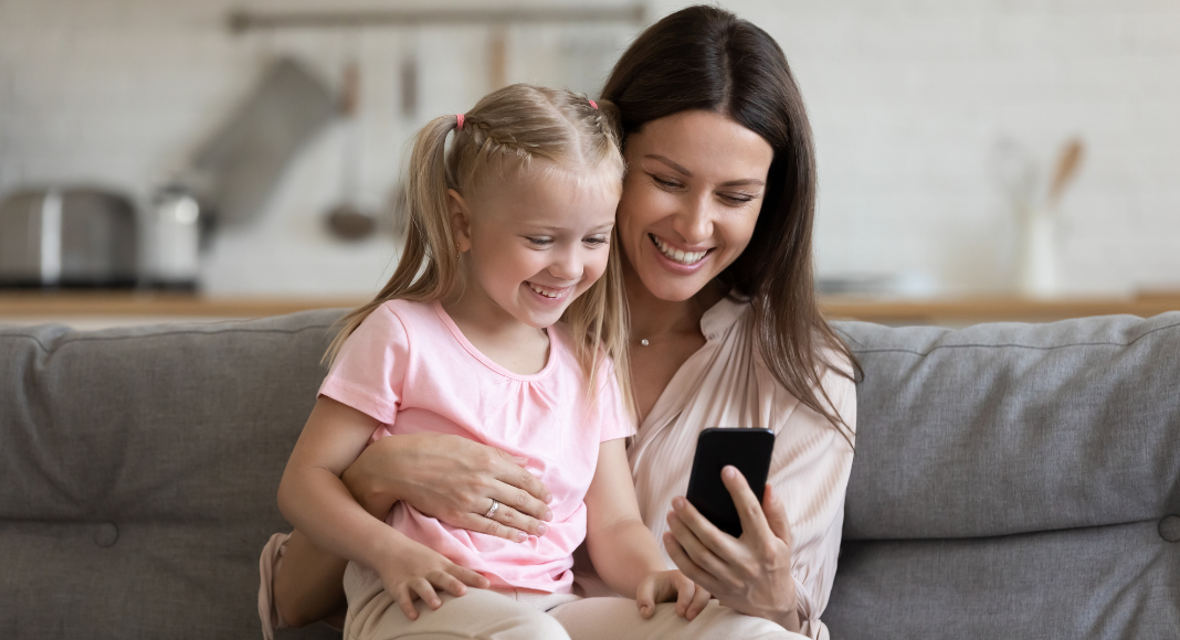 Woman with young child on her lap looks at her phone