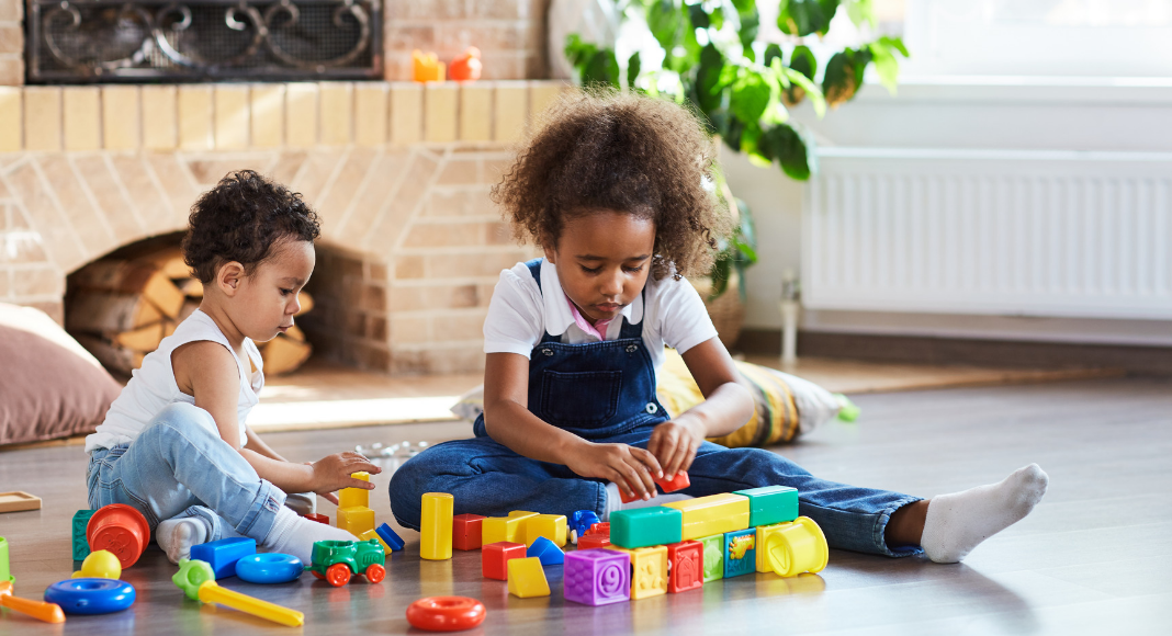 Preschool girl and toddler boy sit on floor playing with blocks