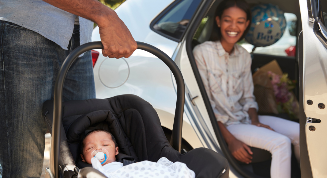 woman smiling at newborn in carseat