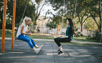 mom friends sit opposite each other on playground swings