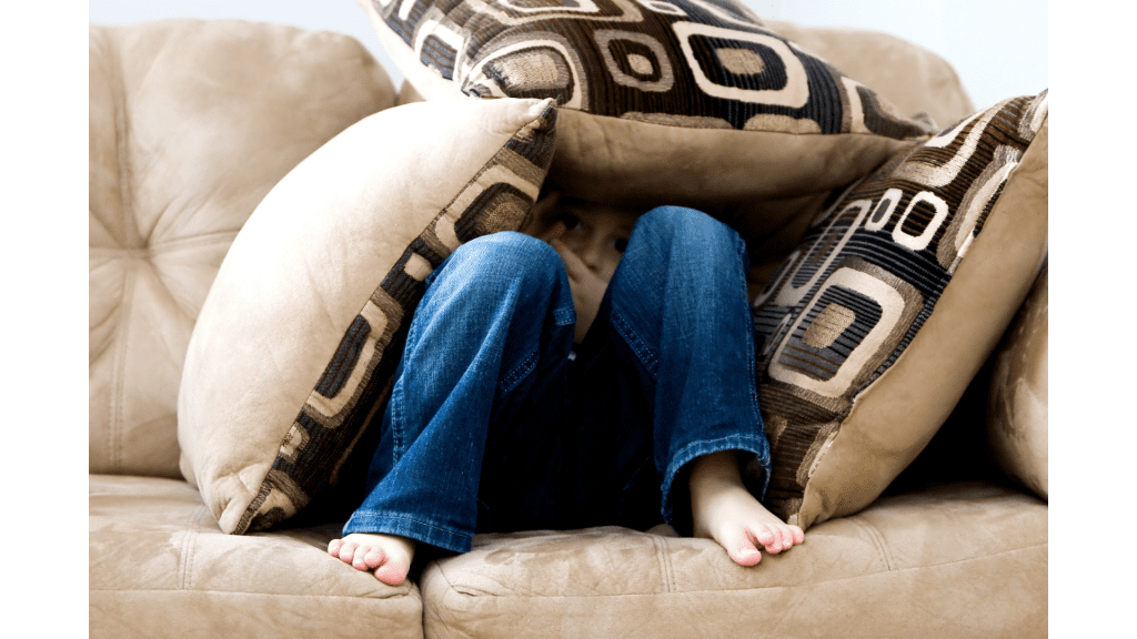 child sitting on couch hiding under throw pillows