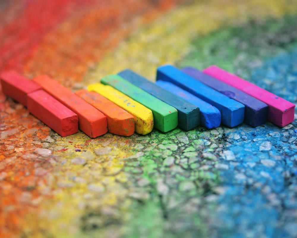 sticks of chalk in rainbow order on top of chalk drawing of a rainbow