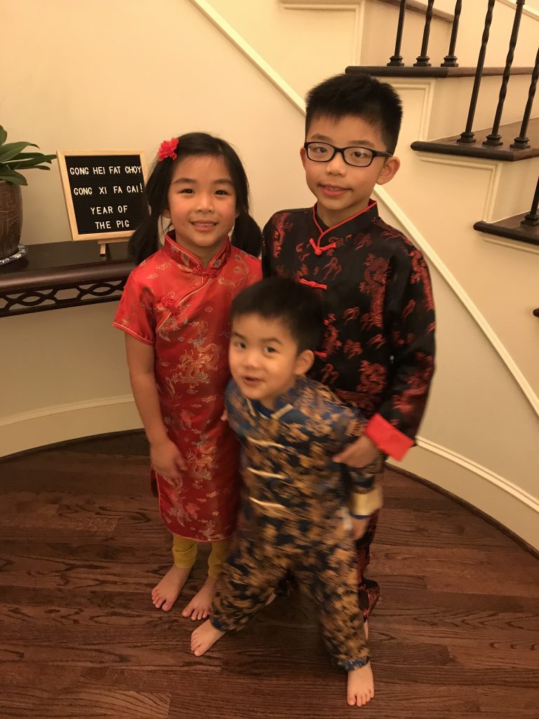 Three young children stand in traditional Chinese heritage clothing