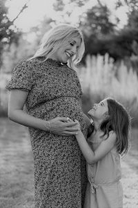 pregnant woman stands with daughter, holding her hand