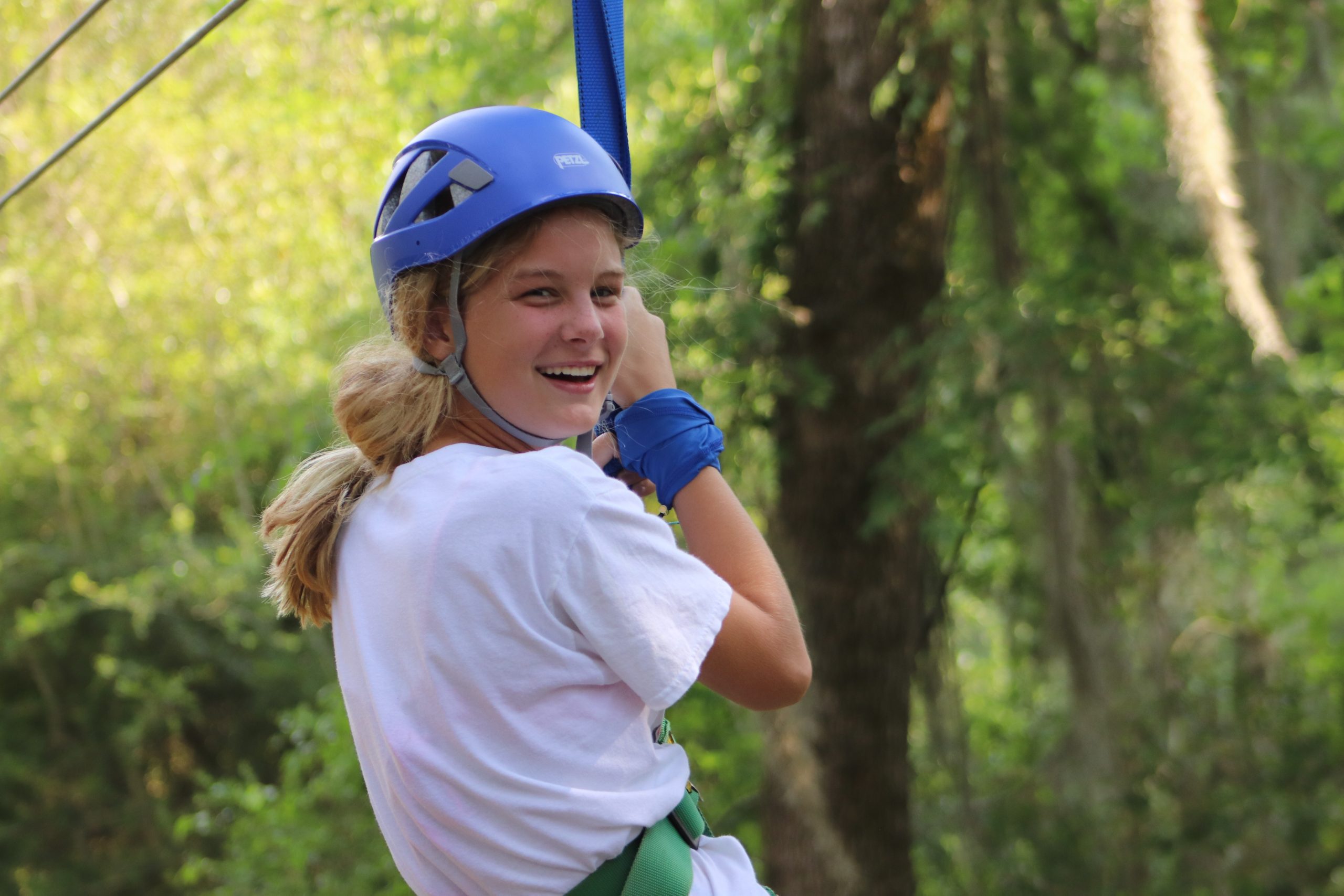 girl with helmet hangs from rope on ropes course