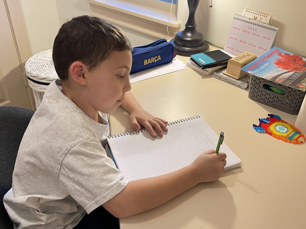 boy sits at desk writing in notebook