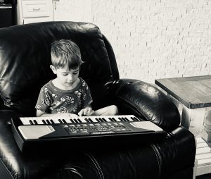 young boy sits in chair playing keyboard