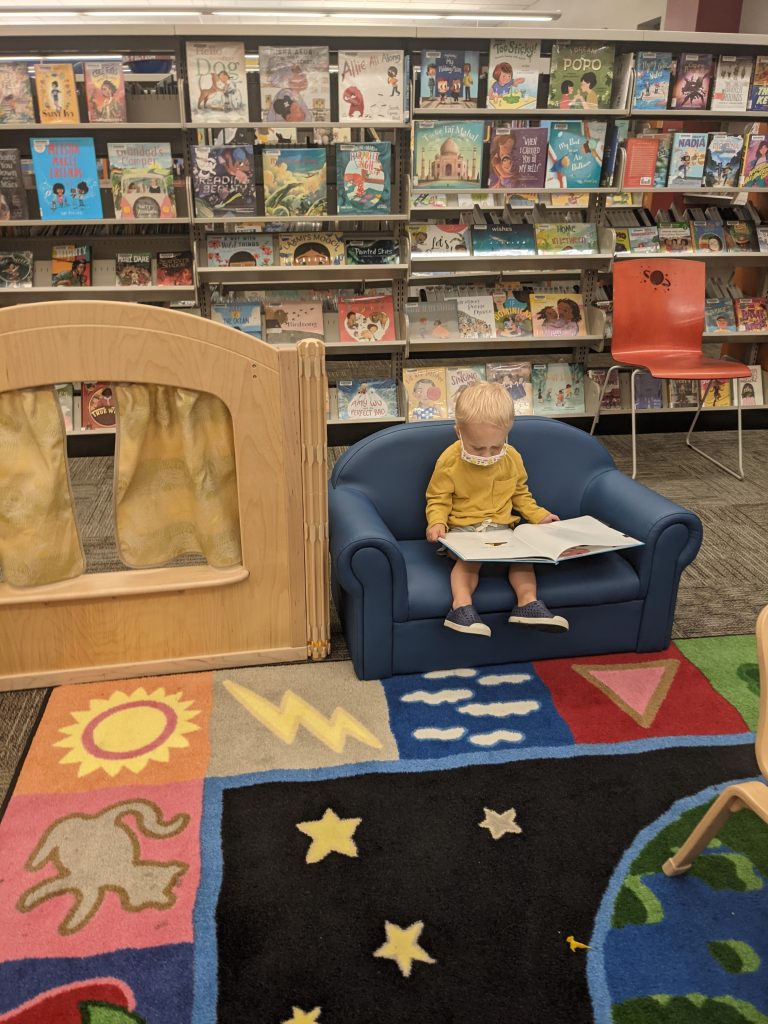 toddler sits on chair at library looking at book