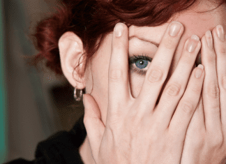 highly sensitive woman peeks through hands covering her face