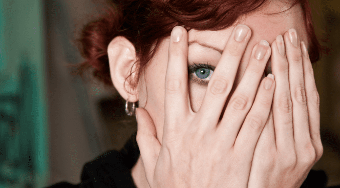 highly sensitive woman peeks through hands covering her face