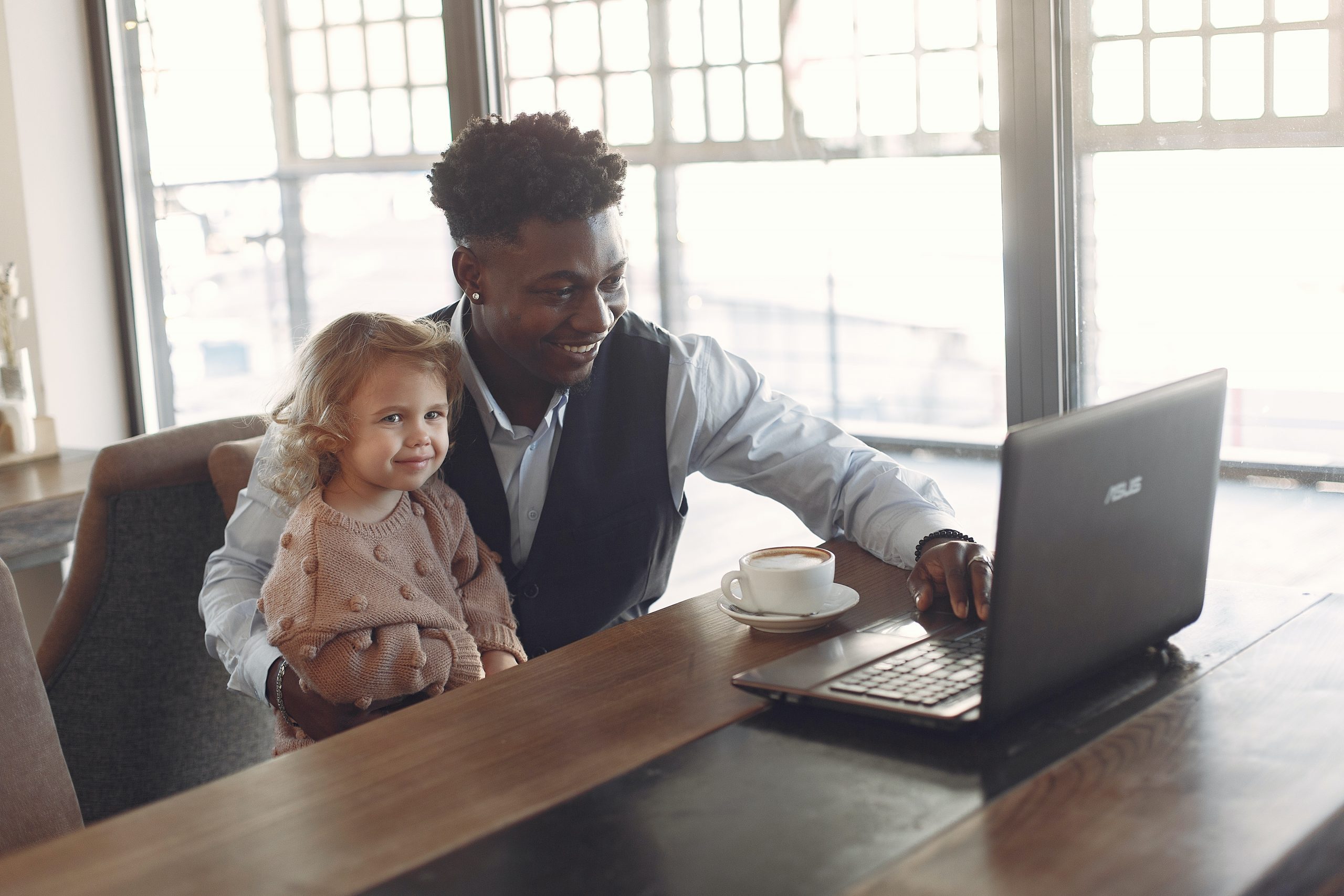 young man holding a toddler on his lap while looking at laptop