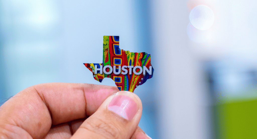 hand holding a tiny pin of shape of Texas with Houston