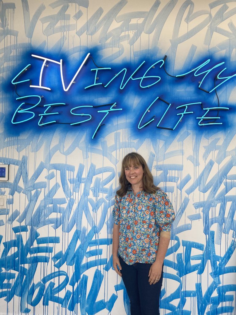 woman stands in front of wall that says "LIVing My Best Life"