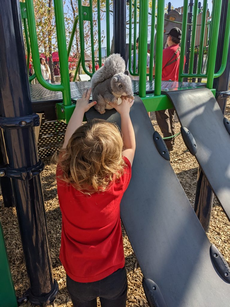 small child holds a stuffed squirrel on the playground