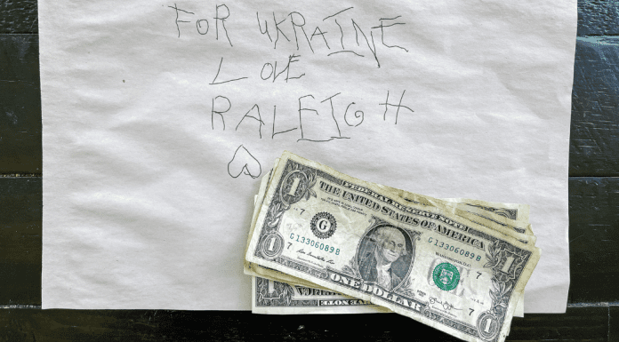A note in a child's writing with the text: For Ukraine love Raleigh. Four 1 dollar bills are on top of the note.
