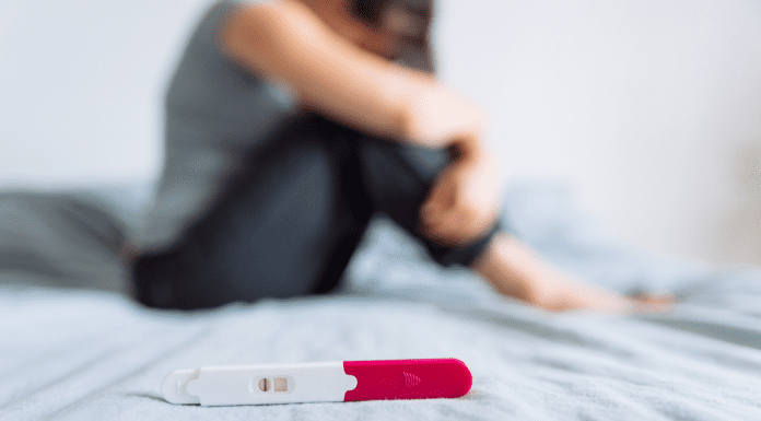 woman sits on bed in front of negative pregnancy test