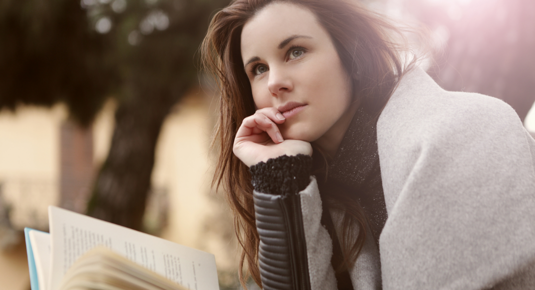 woman with pensive look sits with a book