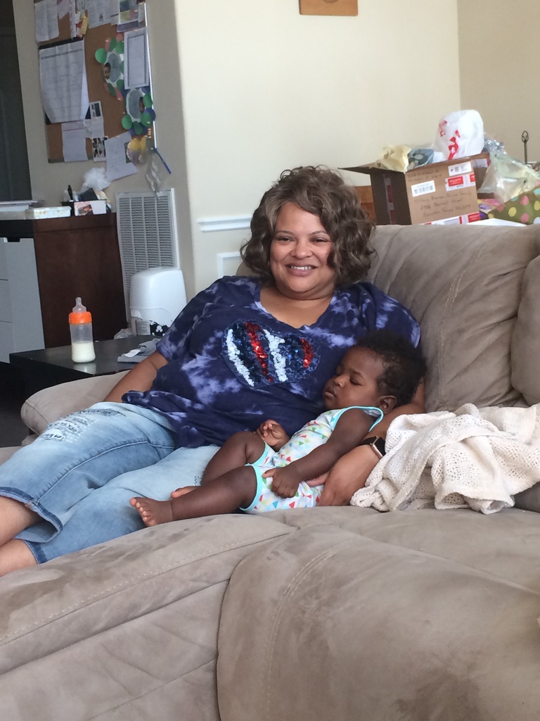 A mother-ish mature friend cuddles a sleeping baby on couch