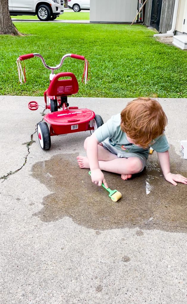 child paints driveway using a roller brush and water