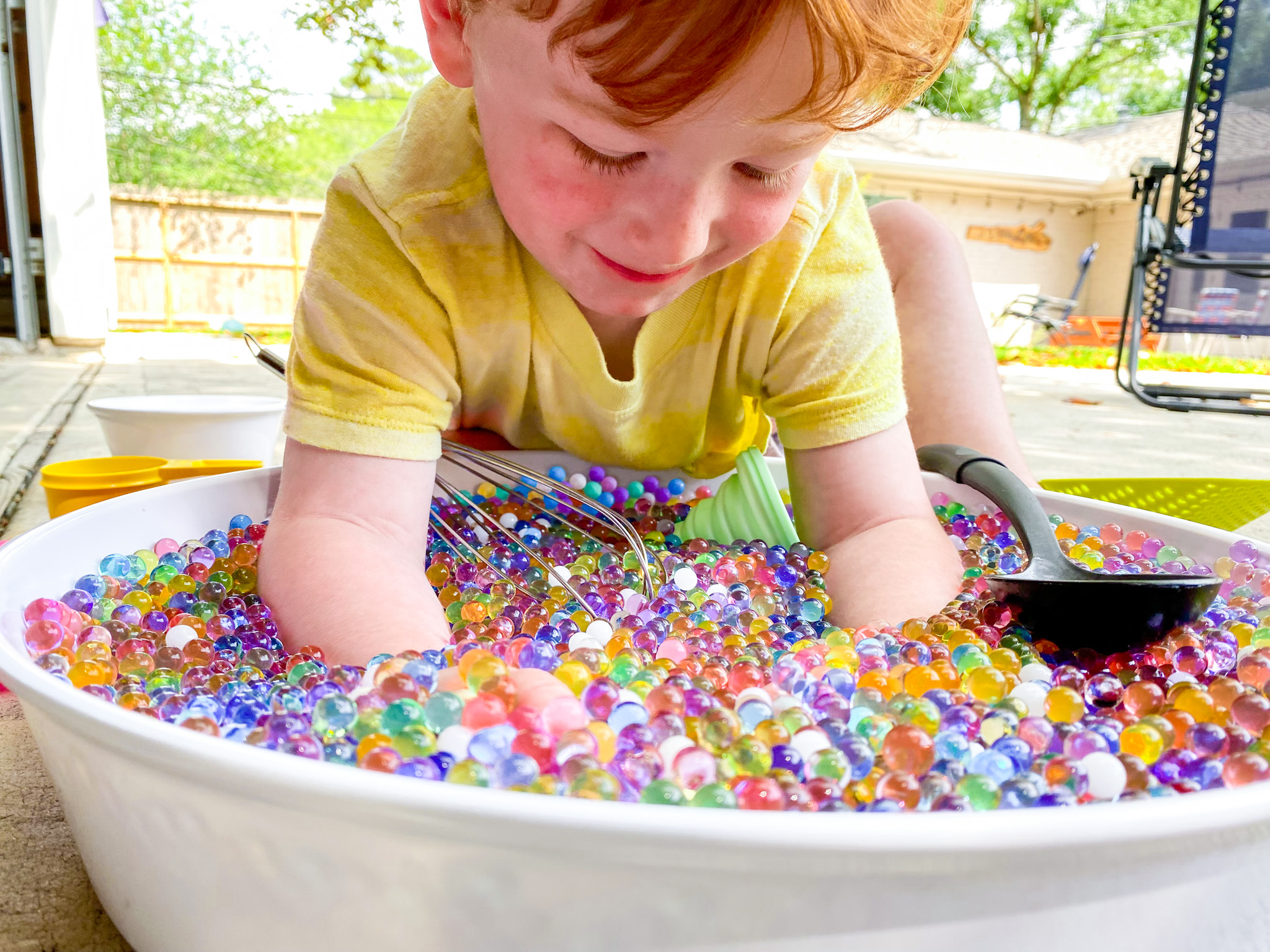 child with arms in bowl of water beads