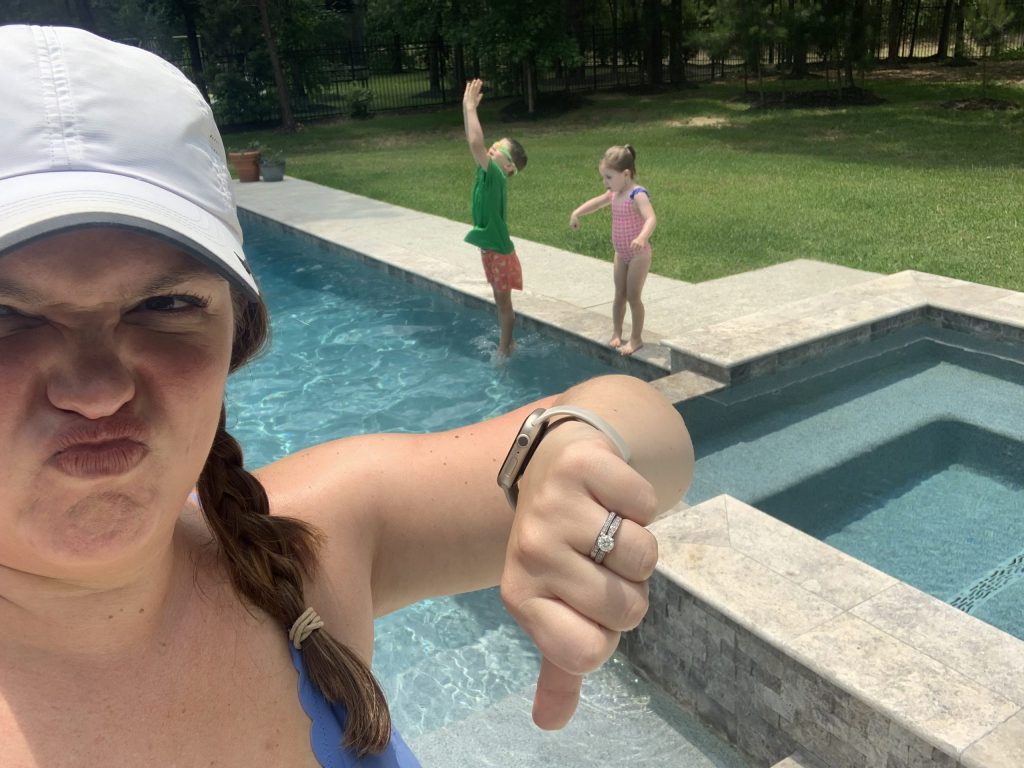 woman with unhappy expression gives a thumbs down as her children play in pool behind her