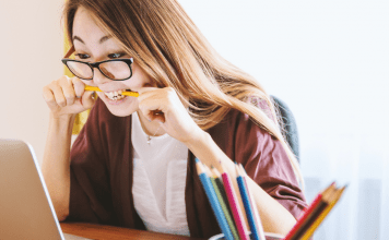 woman chews on pencil while looking at computer
