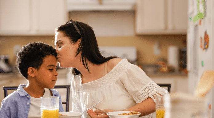mother kisses son on his head at the breakfast table