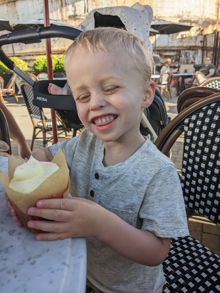 smiling child holding dessert at outdoor table