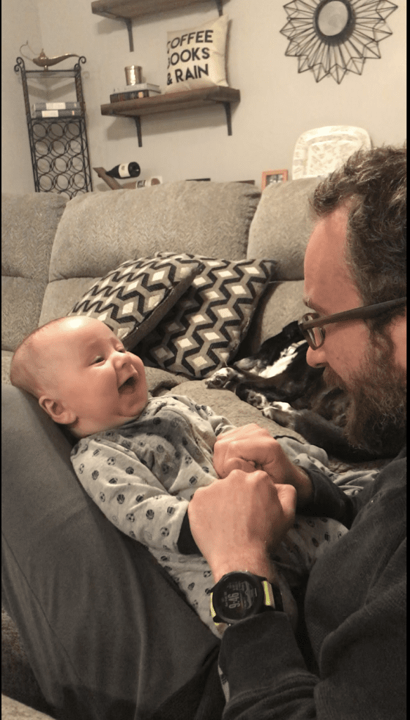 father holds baby with dog lying next to them