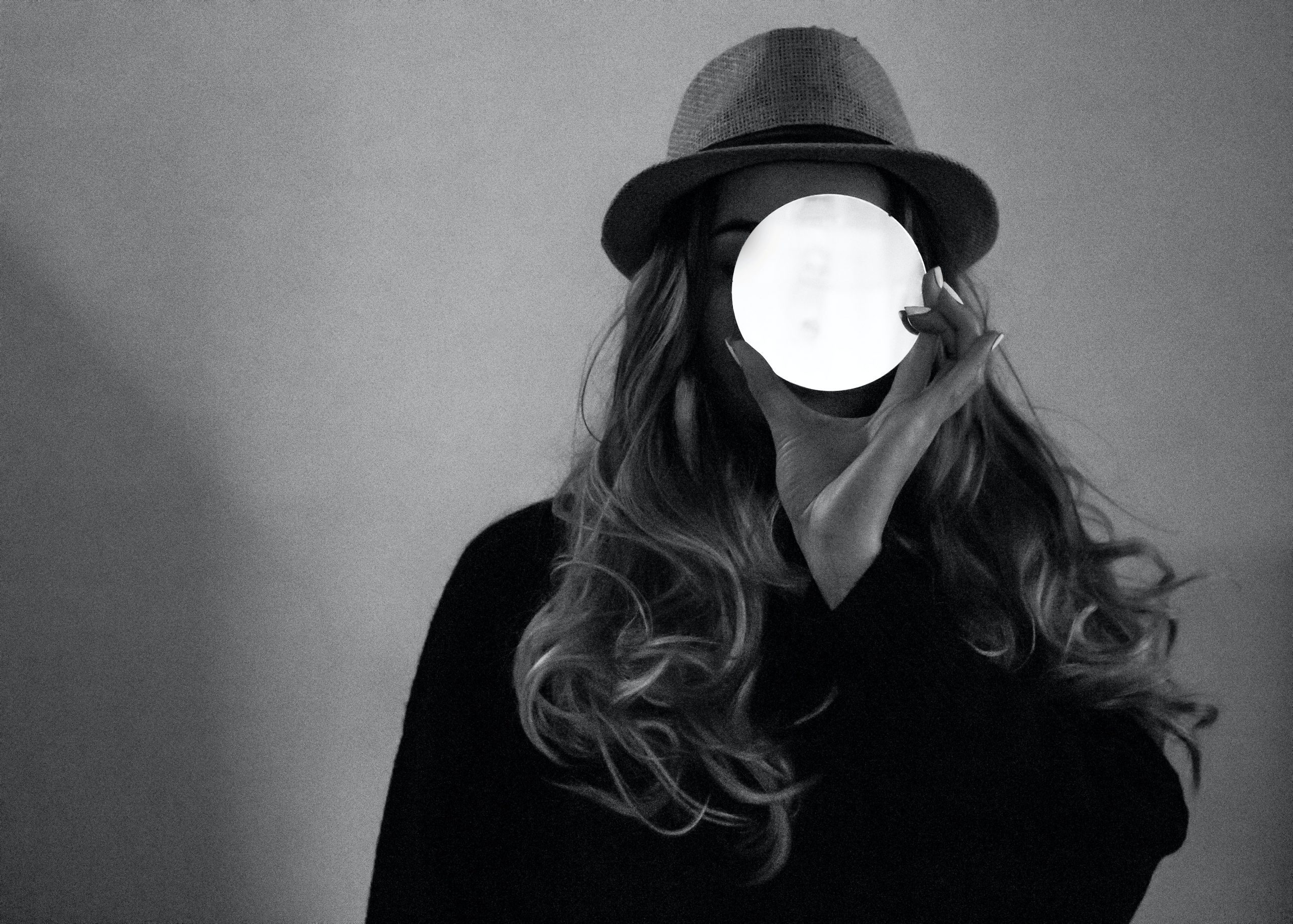 black and white photo of woman holding glowing white circle over face