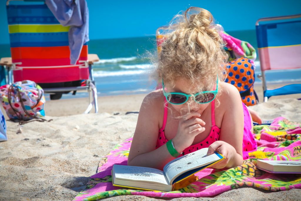 young girl reads book on the beach