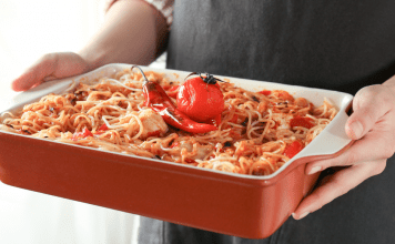 woman's hands hold a casserole dish of spaghetti