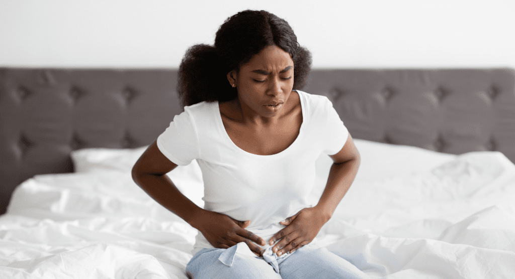 woman sits on bed in pain clutching stomach