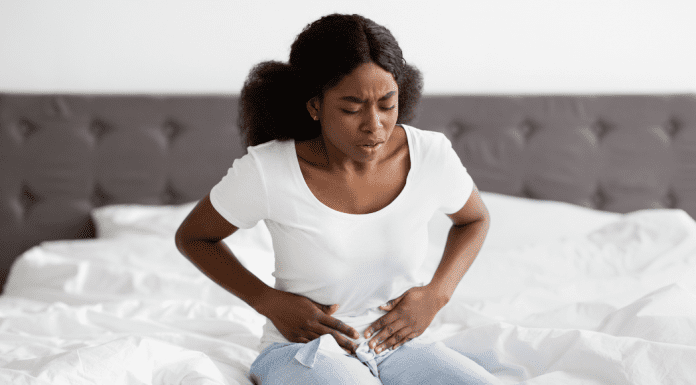woman sits on bed in pain clutching stomach