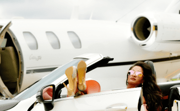 woman in convertible with feet up poses by private jet